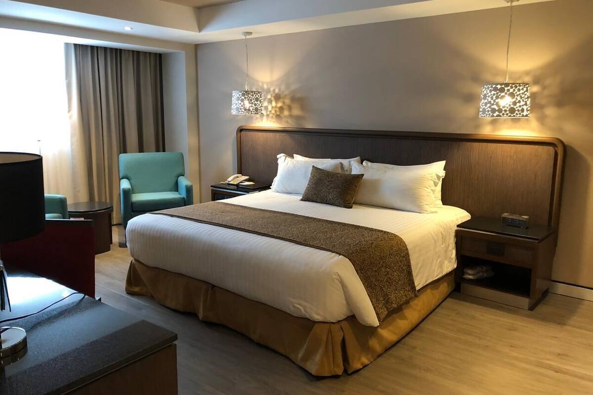 A hotel room with a large bed, a desk, a chair, a nightstand, and a lamp.