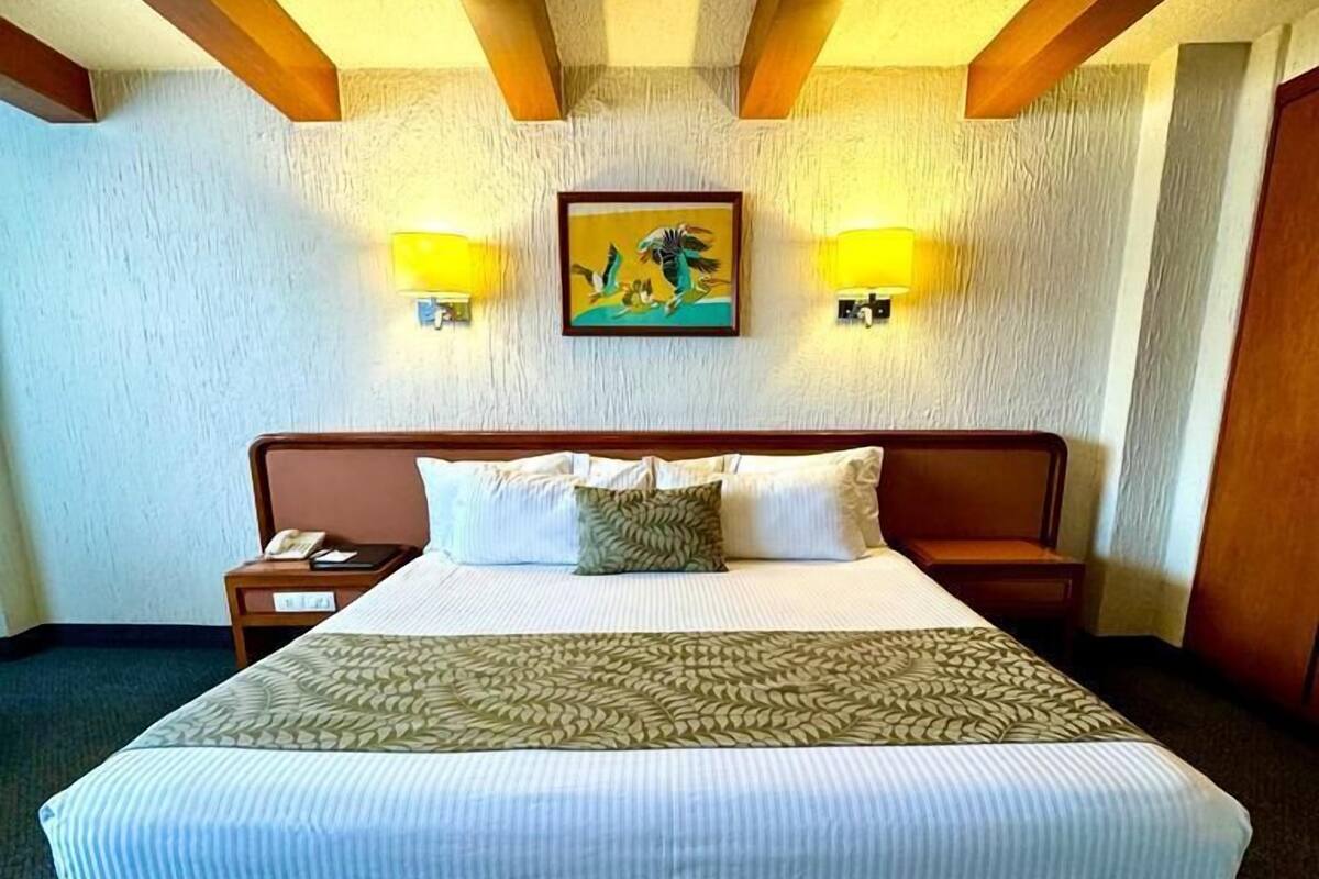 A hotel room with a large bed, two bedside lamps, a painting on the wall, and a wooden ceiling structure.