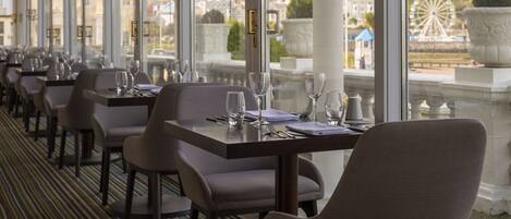 A restaurant with a long table layout, large windows, and a view of a Ferris wheel and buildings.