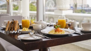 A breakfast table with plates of food, glasses of orange juice, and a view of a Ferris wheel through large windows. - St George's Hotel (Llandudno)