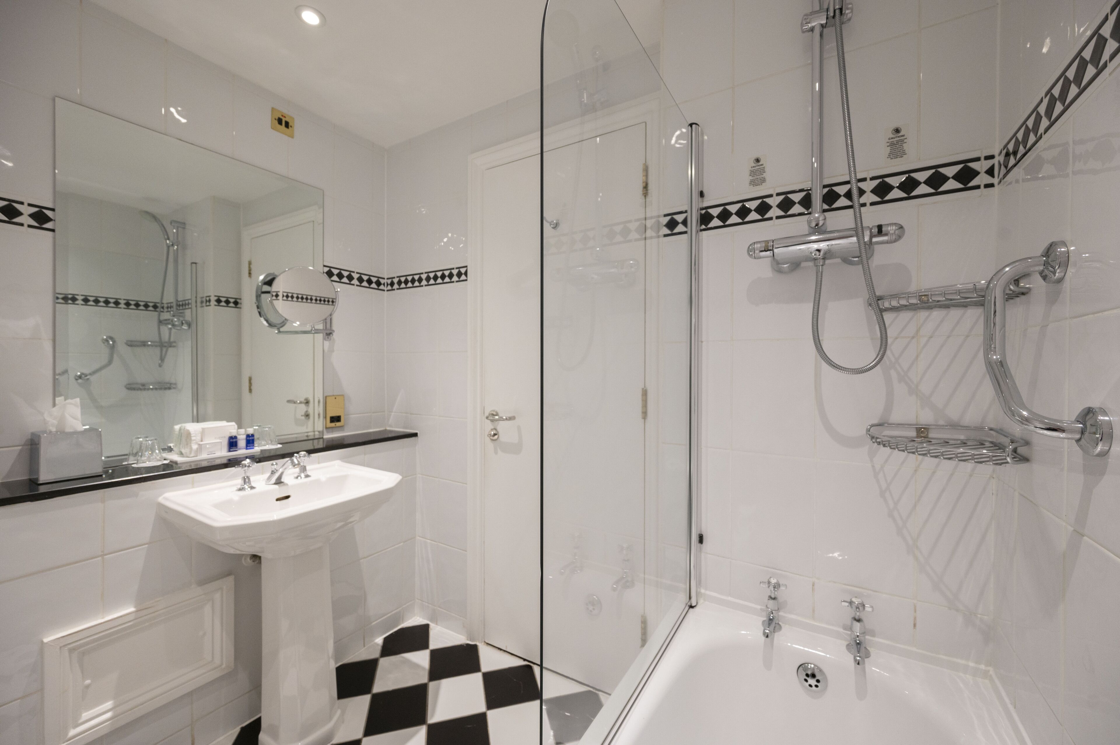 A modern bathroom with a glass-enclosed shower, a white sink, and a checkered floor.