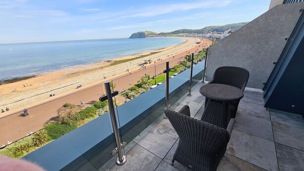 A balcony with wicker chairs and a view of a beach and ocean. - St George's Hotel (Llandudno)