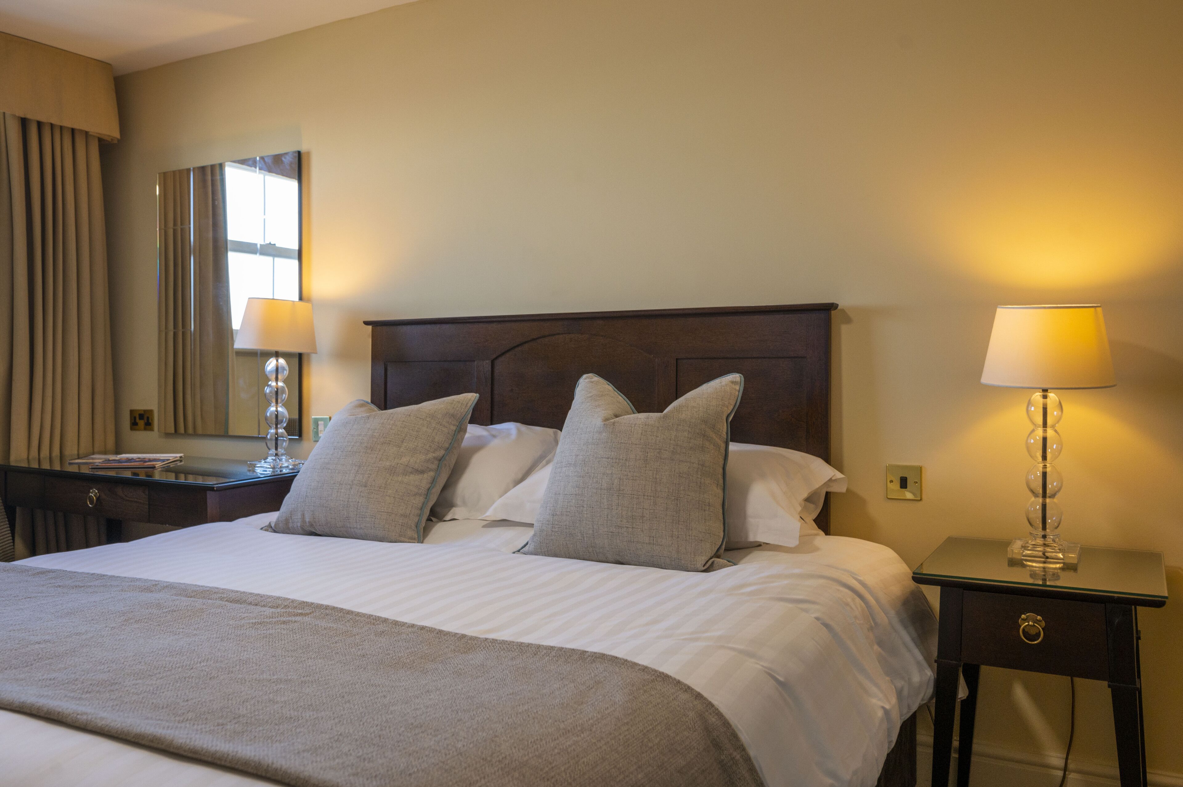 Una cama bien hecha con cabecera de madera, dos lámparas de noche y una mesita de noche con lámpara.