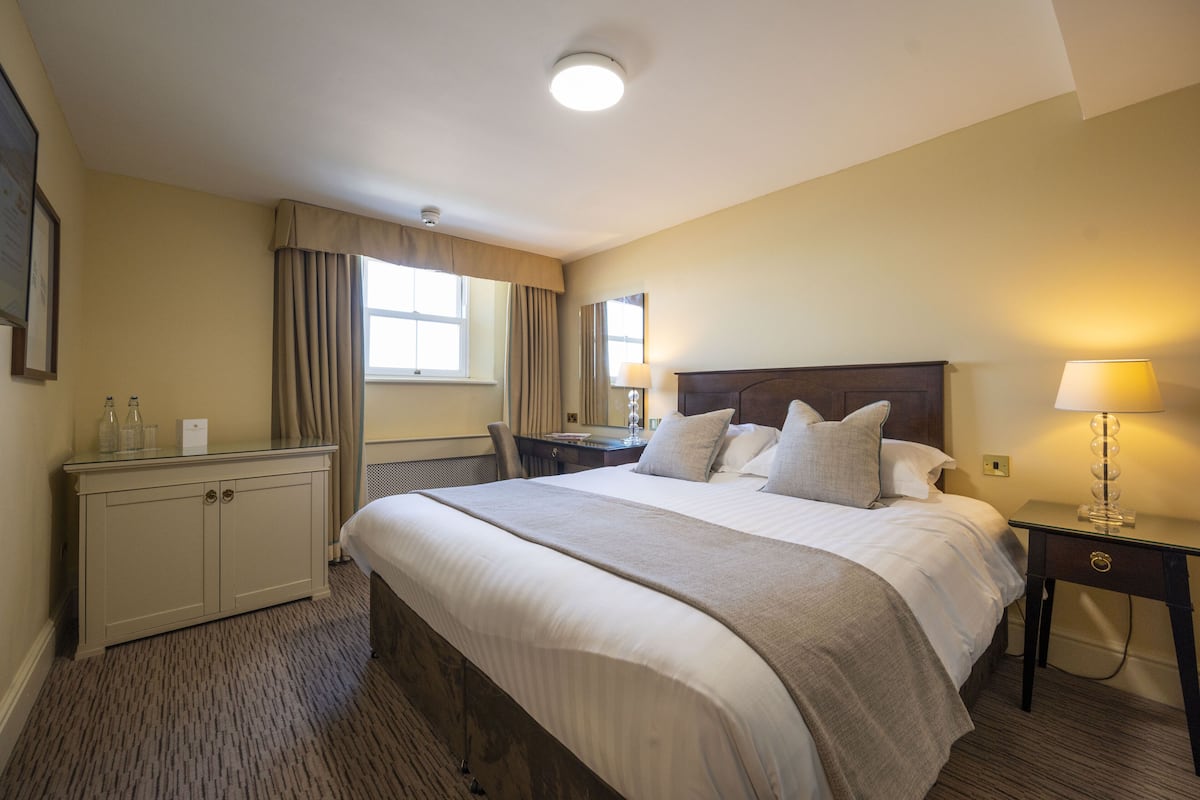 A hotel room with a large bed, bedside tables with lamps, a desk, a chair, and a wardrobe.