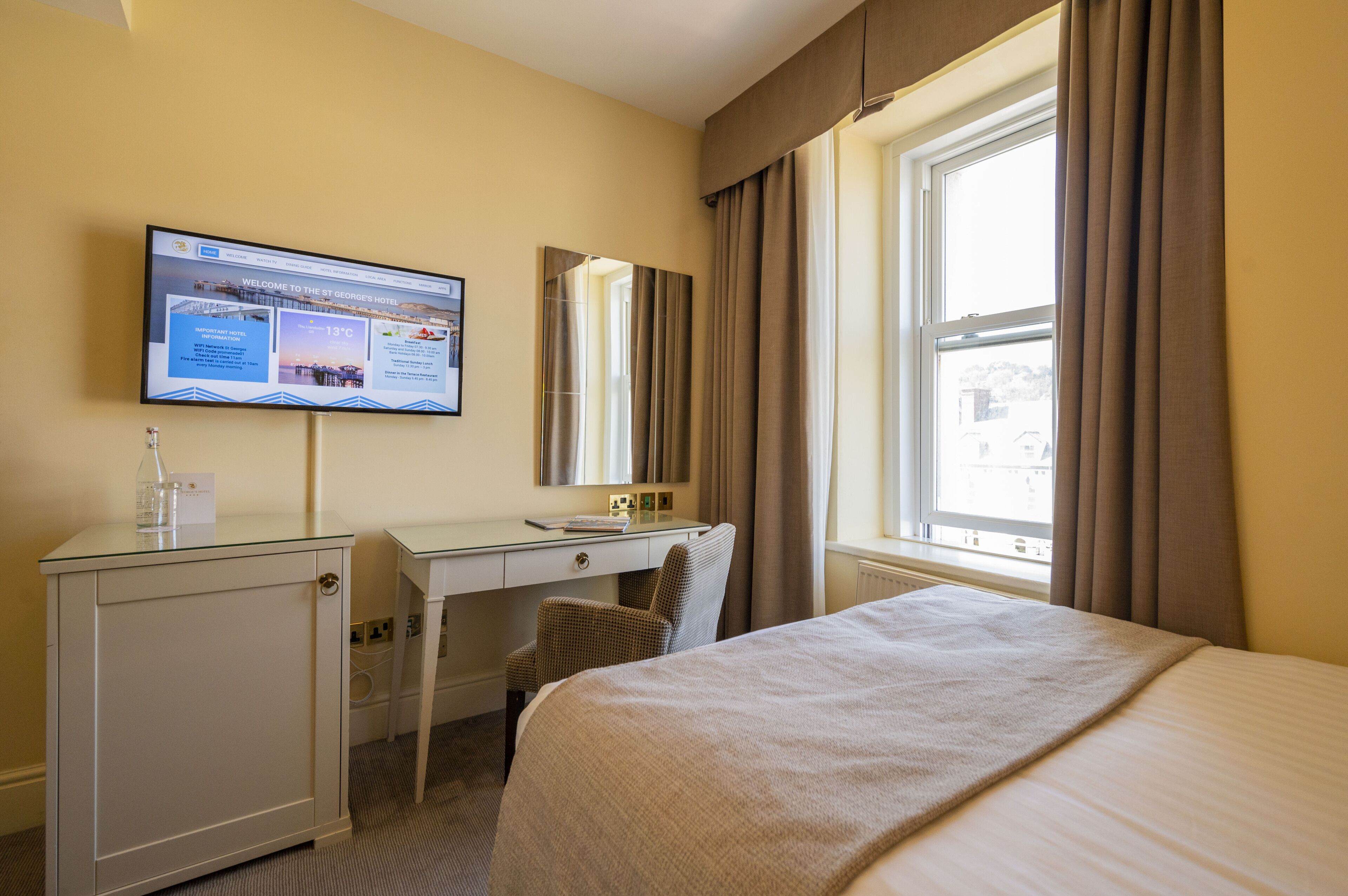 Habitación de hotel con cama, escritorio con silla, televisor y ventana con cortinas.