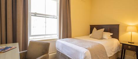 A hotel room with a bed, a chair, a desk, and a lamp.