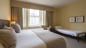 A hotel room with a large bed, a smaller bed, a chair, a desk, and a window with curtains.