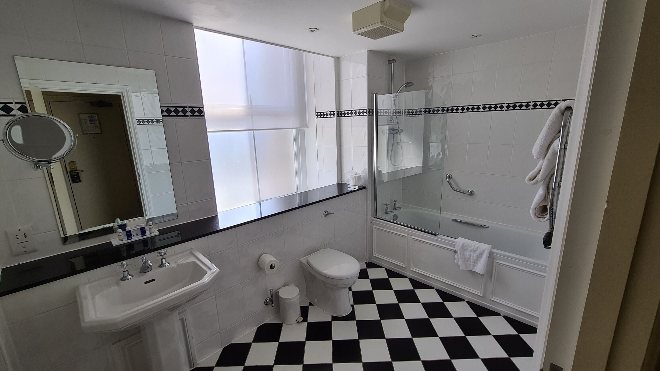 A bathroom with a black and white checkered floor, a white sink, a toilet, a glass shower enclosure, and a mirror with a black countertop.
