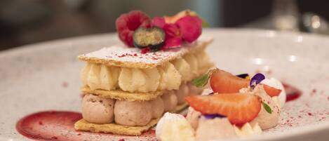 A dessert plate with multiple layers of cream and berries, garnished with flowers and a dusting of powder.