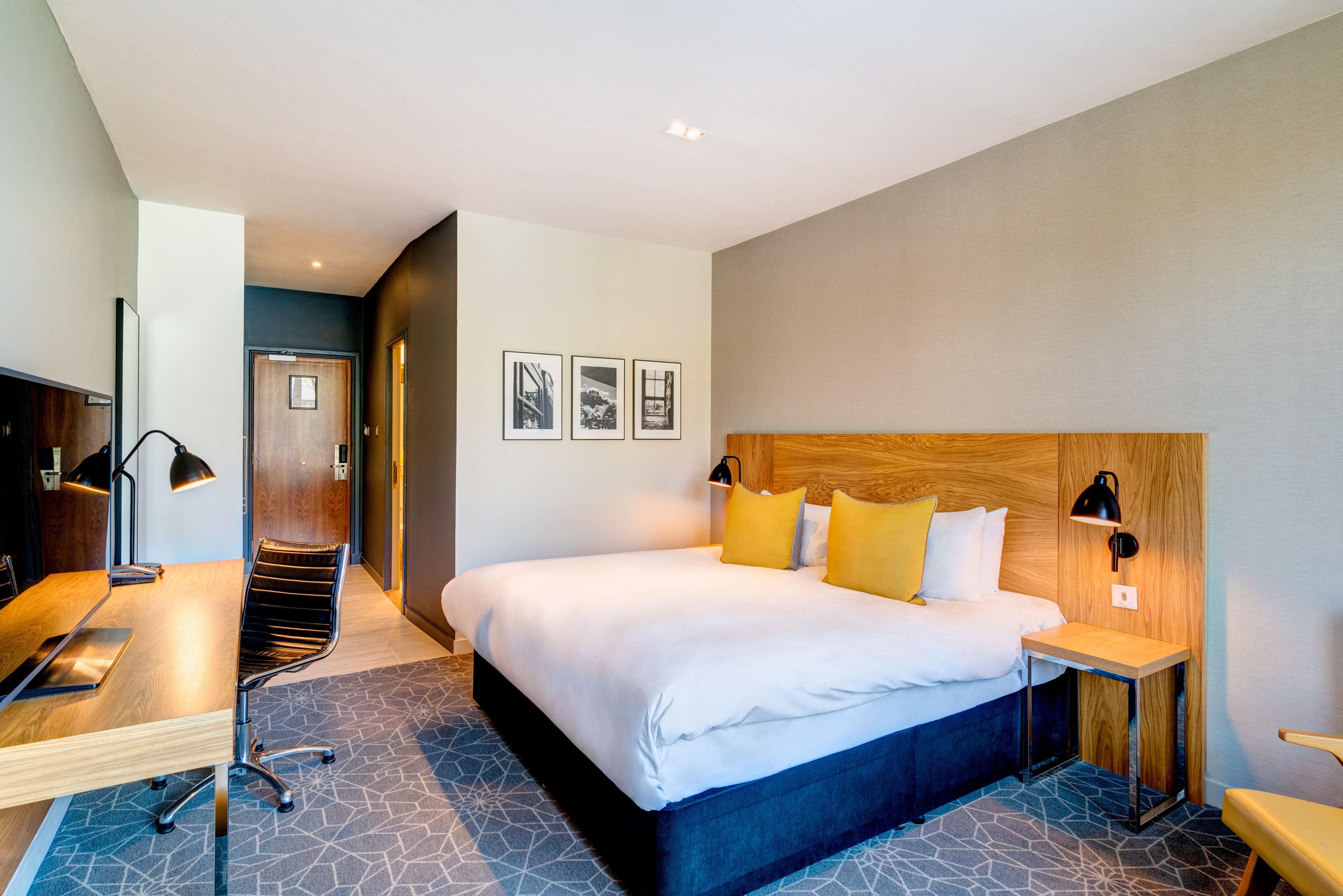 Ein modernes Hotelzimmer mit einem großen Bett, einem Schreibtisch und einem Sessel. An der Wand hängen drei gerahmte Bilder.