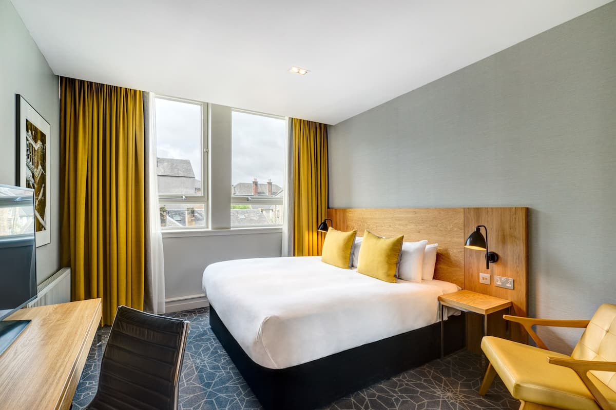 Una habitación de hotel con una cama grande, un escritorio, una silla y vistas a la ciudad desde la ventana.