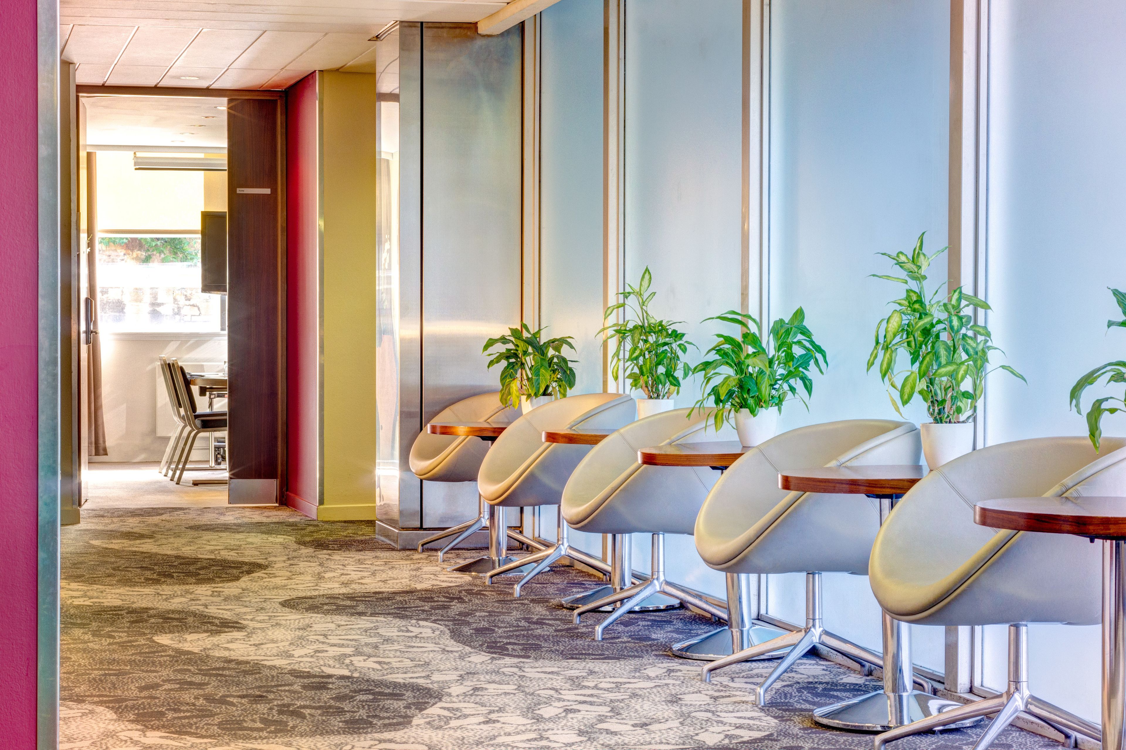 A hotel lobby with a row of modern chairs, a carpeted floor, and a plant wall.