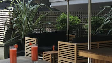 Un espace extérieur aménagé avec des tables et des chaises en bois, des parasols et des plantes en pot.