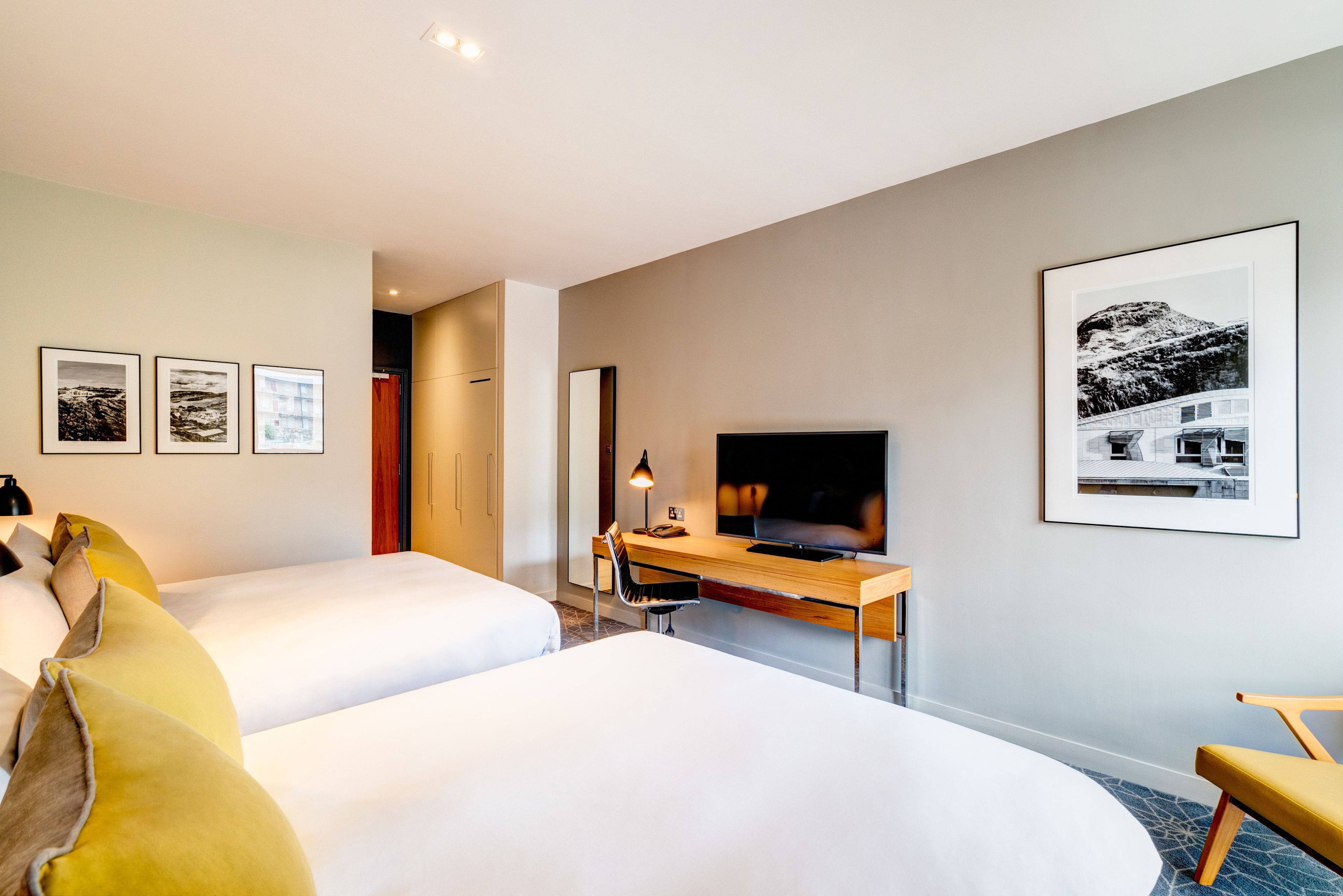 A hotel room with two beds, a desk with a TV, and framed pictures on the walls.