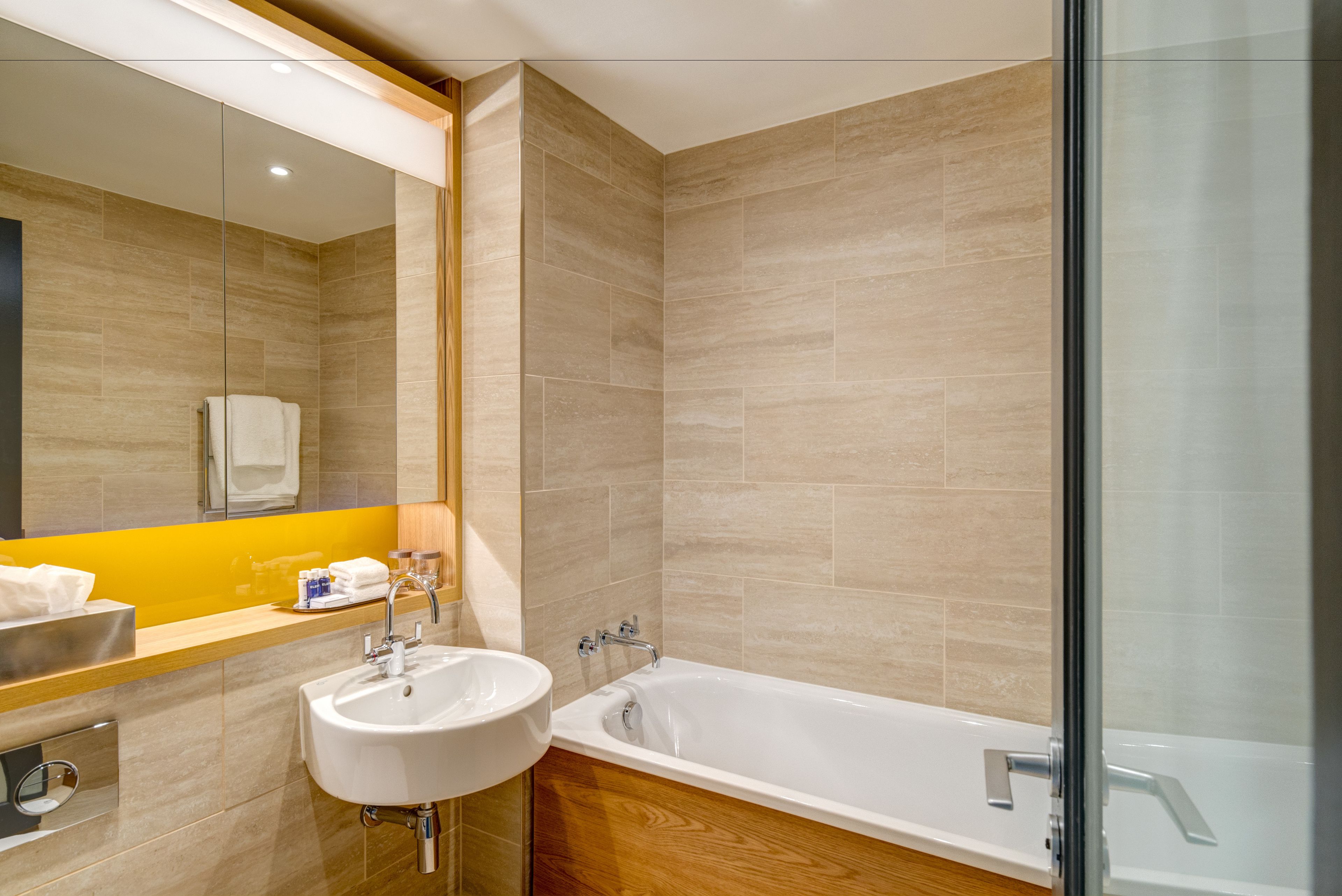 A modern bathroom with a large mirror, a sink, and a bathtub.