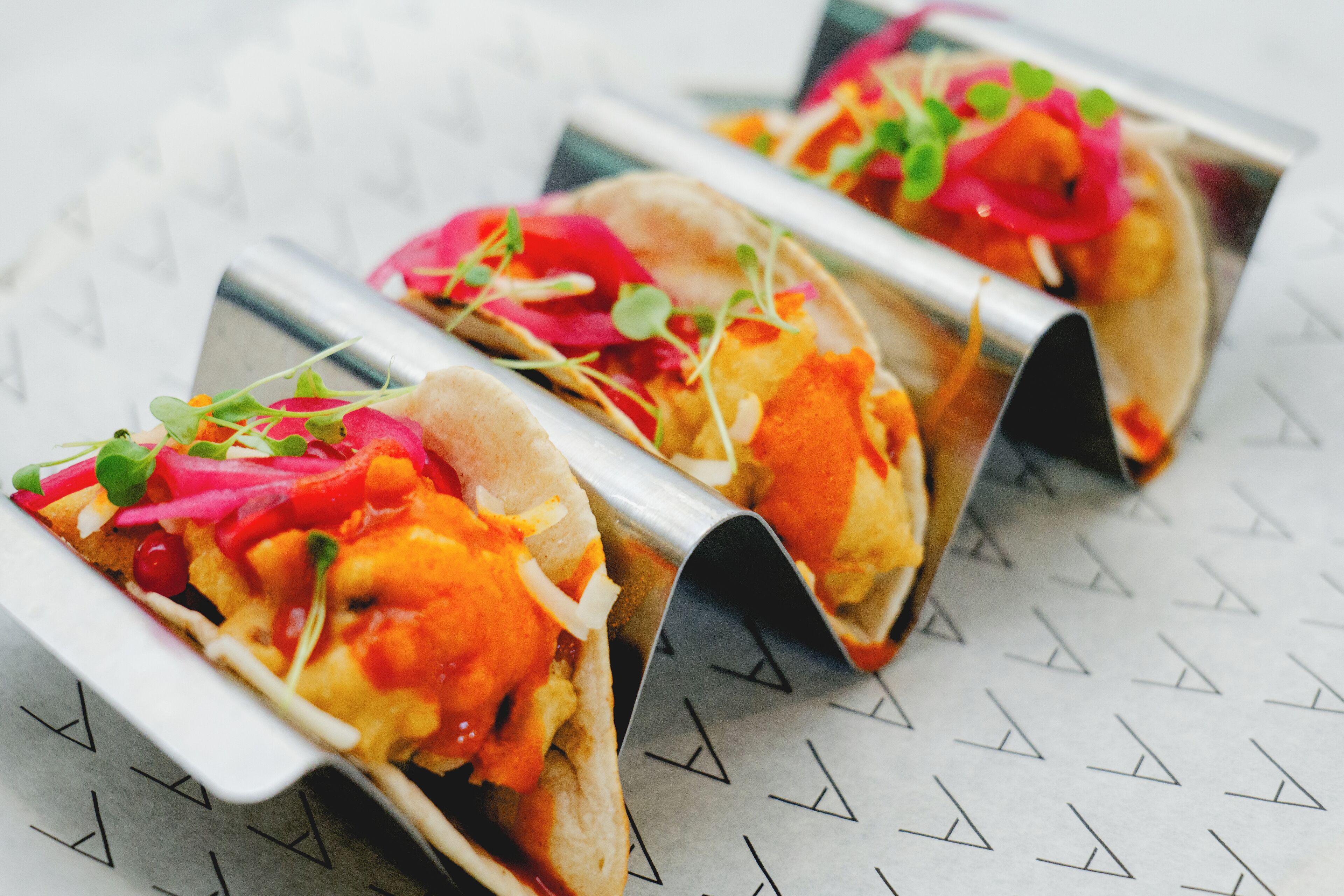 Three tacos with a variety of toppings, including lettuce and possibly cheese, presented on a tray.