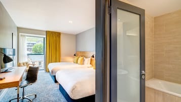 Habitación de hotel con escritorio, dos camas, una silla, televisión y baño con bañera.