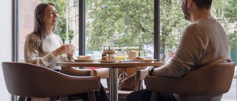 A cafe with a large window, a table with chairs, and a view of buildings and trees.
