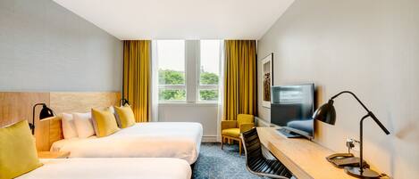 Ein Hotelzimmer mit zwei Betten, einem Schreibtisch, einem Stuhl, einem Fernseher und einem Fenster mit Vorhängen.