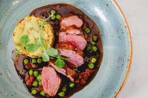 A plate with sliced meat, peas, and a potato.