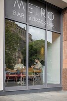 A restaurant with large windows, a sign reading 'METRO BAR & BRASSERIE,' and reflections of people inside.