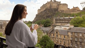 A person holding a cup, overlooking a historic castle with buildings in the foreground. - Apex Grassmarket Hotel (Edinburgh)
