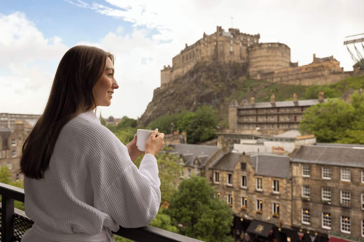Una persona sosteniendo una taza, con vistas a un castillo histórico y edificios en primer plano.