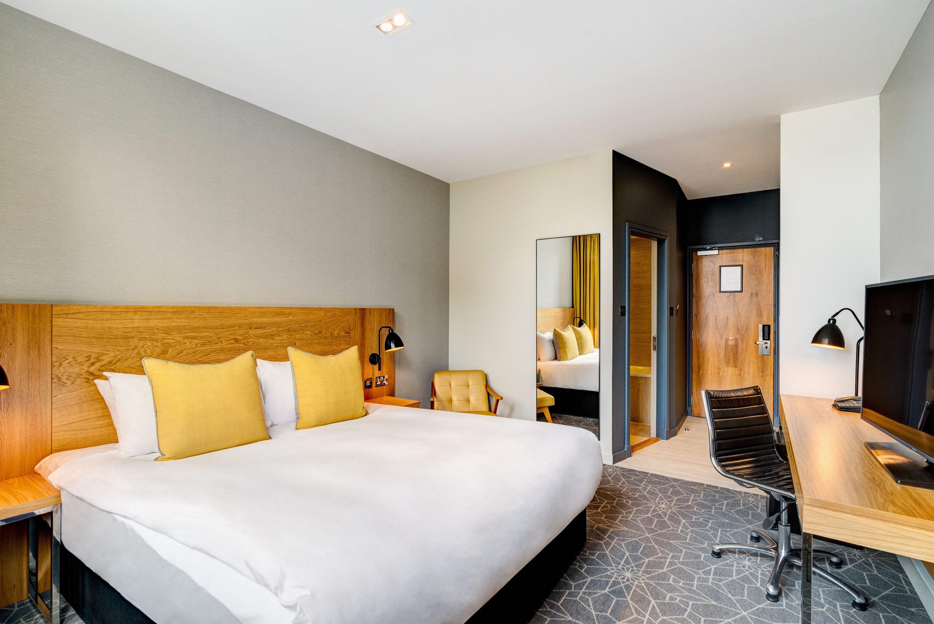 A modern hotel room with a large bed, a desk, a chair, and a television.