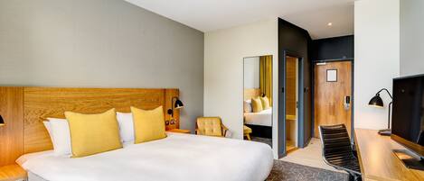 A modern hotel room with a large bed, a desk, a chair, and a television.