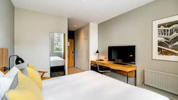 A modern hotel room with a large bed, a desk with a computer, a TV, and a window with a view of a building.