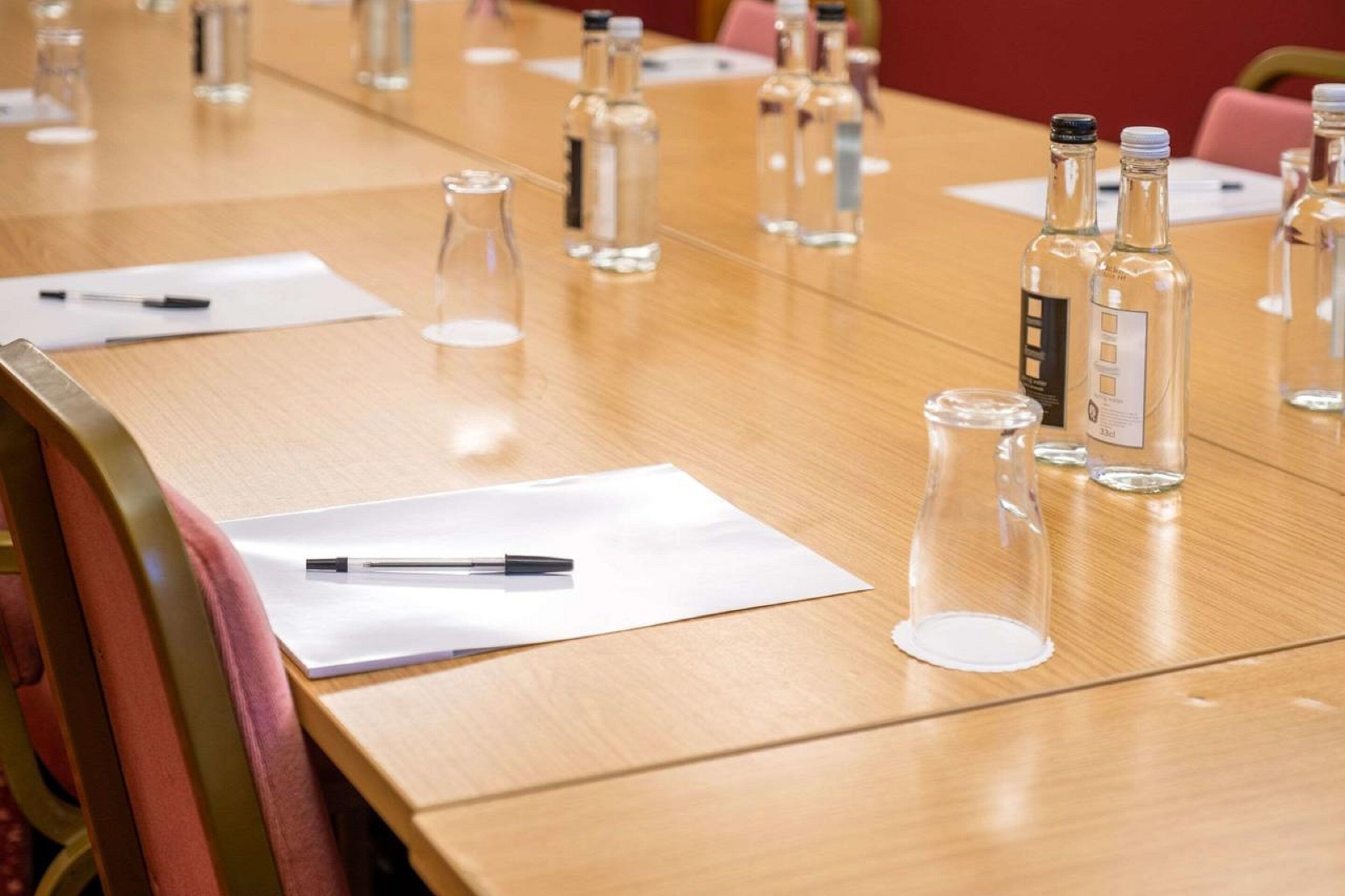 A conference table with clear glass bottles, pens, and papers.