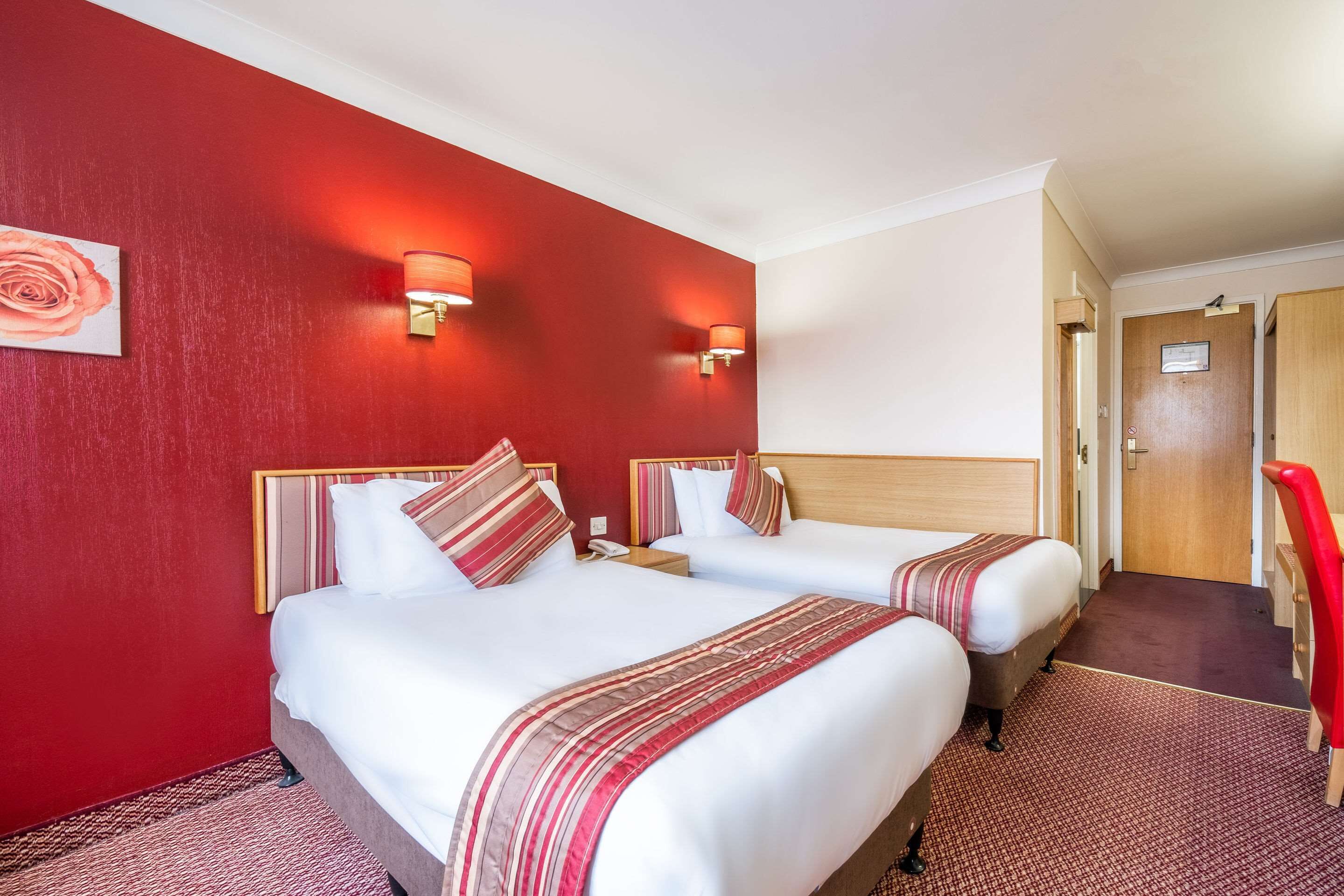 A hotel room with two beds, red walls, and a red carpet.