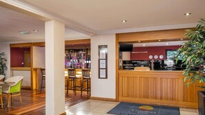 Uma área de recepção de hotel com um balcão de madeira, um bar e assentos.