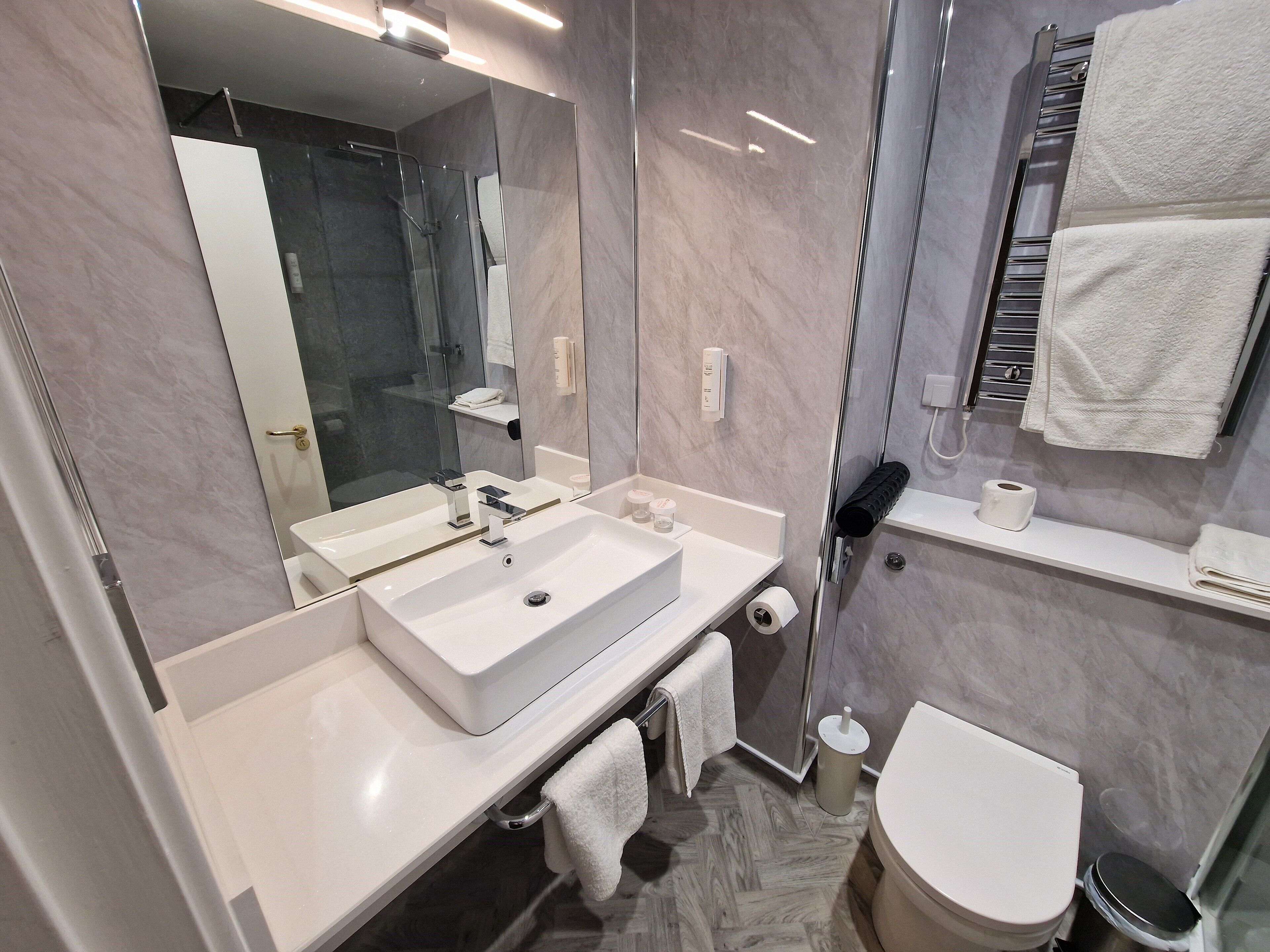 Un baño moderno con un espejo grande, un lavabo blanco y un inodoro.