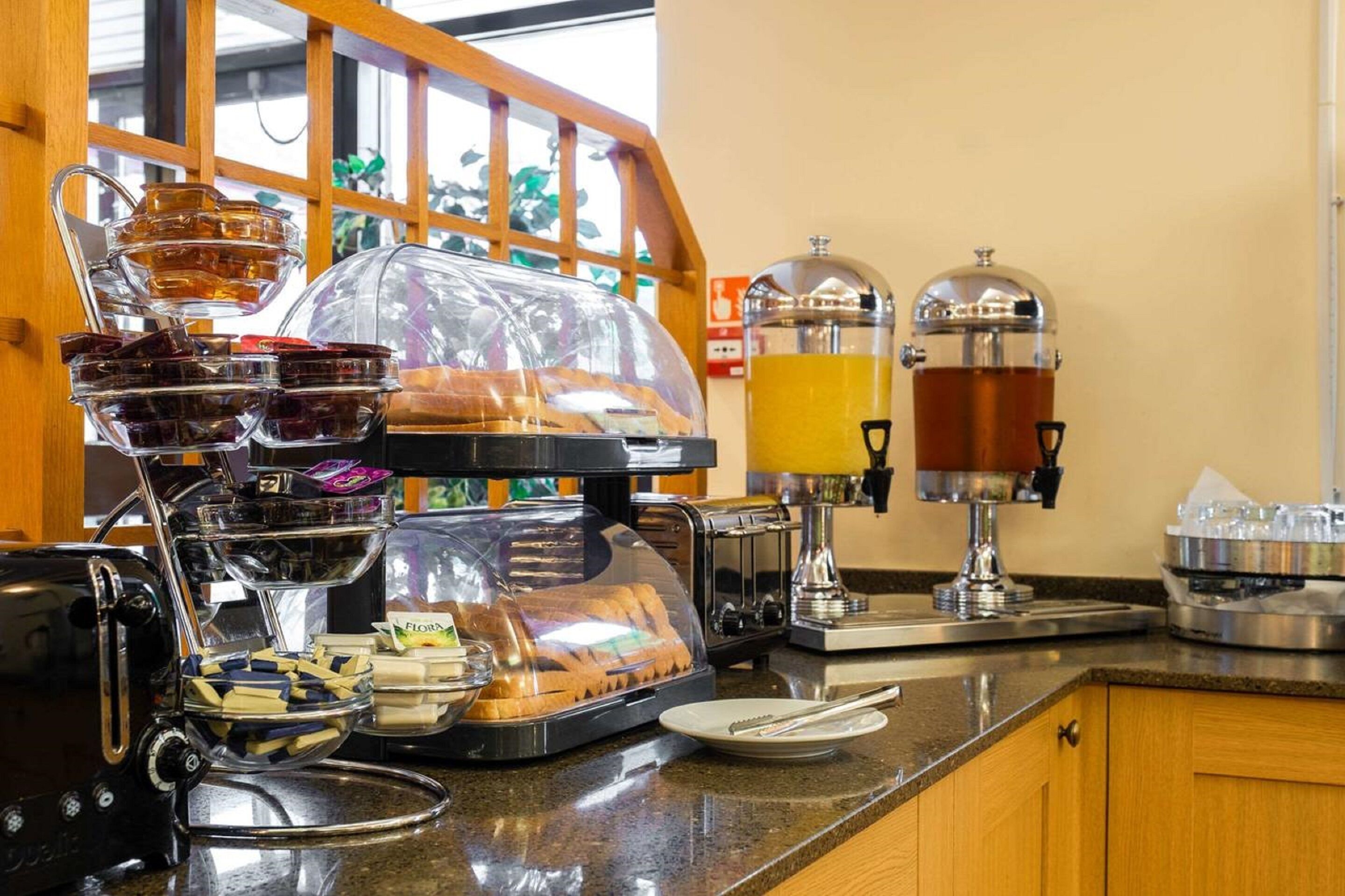 Estación de desayuno con máquina de café, dispensador de jugo y exhibición de pan.