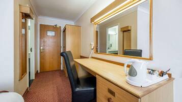 Une chambre d’hôtel avec un bureau en bois, une chaise de bureau noire, une bouilloire blanche et un grand miroir.