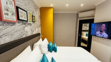 A hotel room with a bed, pillows, a television, and framed pictures on the wall.