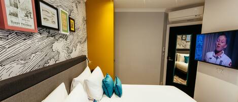 A hotel room with a bed, pillows, a television, and framed pictures on the wall.