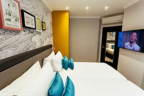 Quarto de hotel com cama, almofadas, televisão e quadros nas paredes.