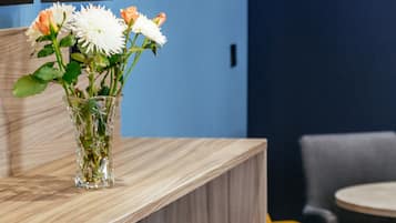 Una zona de bar con un jarrón de cristal transparente que contiene flores sobre una encimera de madera, taburetes de bar grises y amarillos, y cuadros en la pared.