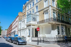 A row of parked cars in front of a hotel with a white facade and a black wrought iron fence. - Oliver Plaza (London)