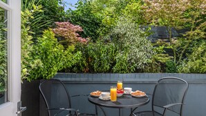 A patio with a table set for breakfast, surrounded by lush greenery and a stone wall. - The Resident Kensington (London)