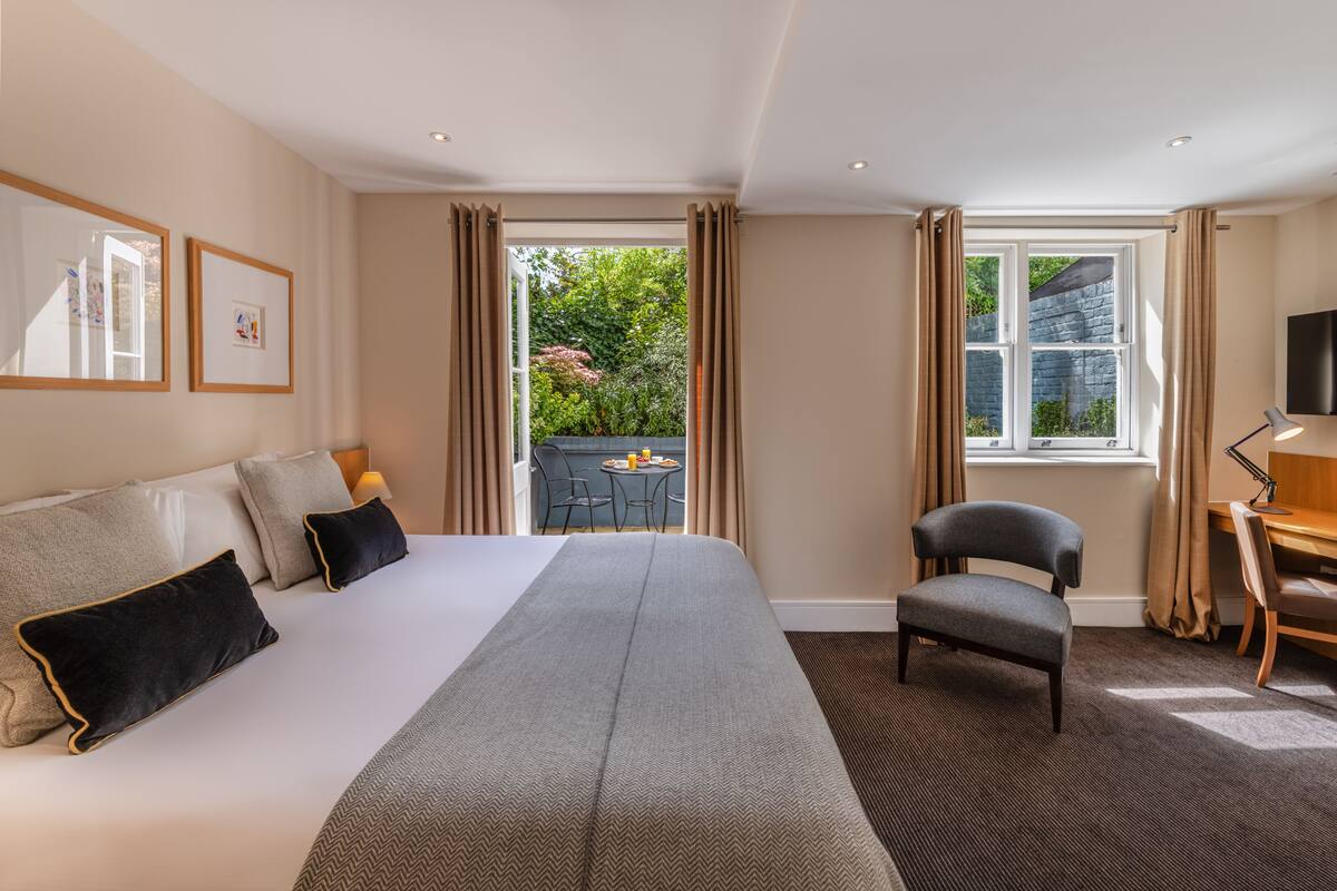 A hotel room with a large bed, a desk, a chair, and a view of the outdoors.