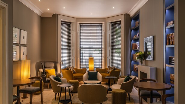 A modern living room with a fireplace, comfortable seating, and bookshelves. - The Resident Kensington (London)
