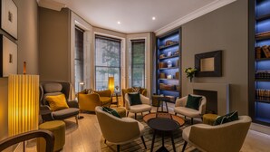 A modern living room with a fireplace, bookshelves, and comfortable seating. - The Resident Kensington (London)