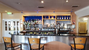 A bar area with a stainless steel counter, multiple seating options, and a variety of bottles and glasses on shelves. - Roundhouse Hotel Bournemouth (Bournemouth)