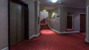 A hallway with a red carpet, an elevator, a staircase, and a door with a mirror. - Roundhouse Hotel Bournemouth (Bournemouth)