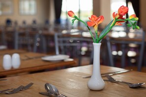 A dining table with a white vase containing orange flowers, cutlery, and salt and pepper shakers. - Roundhouse Hotel Bournemouth (Bournemouth)
