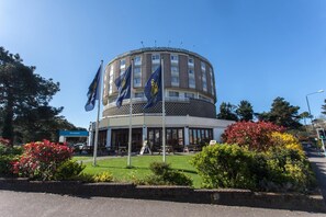 A round building with multiple flags, a reception area, and a landscaped garden. - Roundhouse Hotel Bournemouth (Bournemouth)