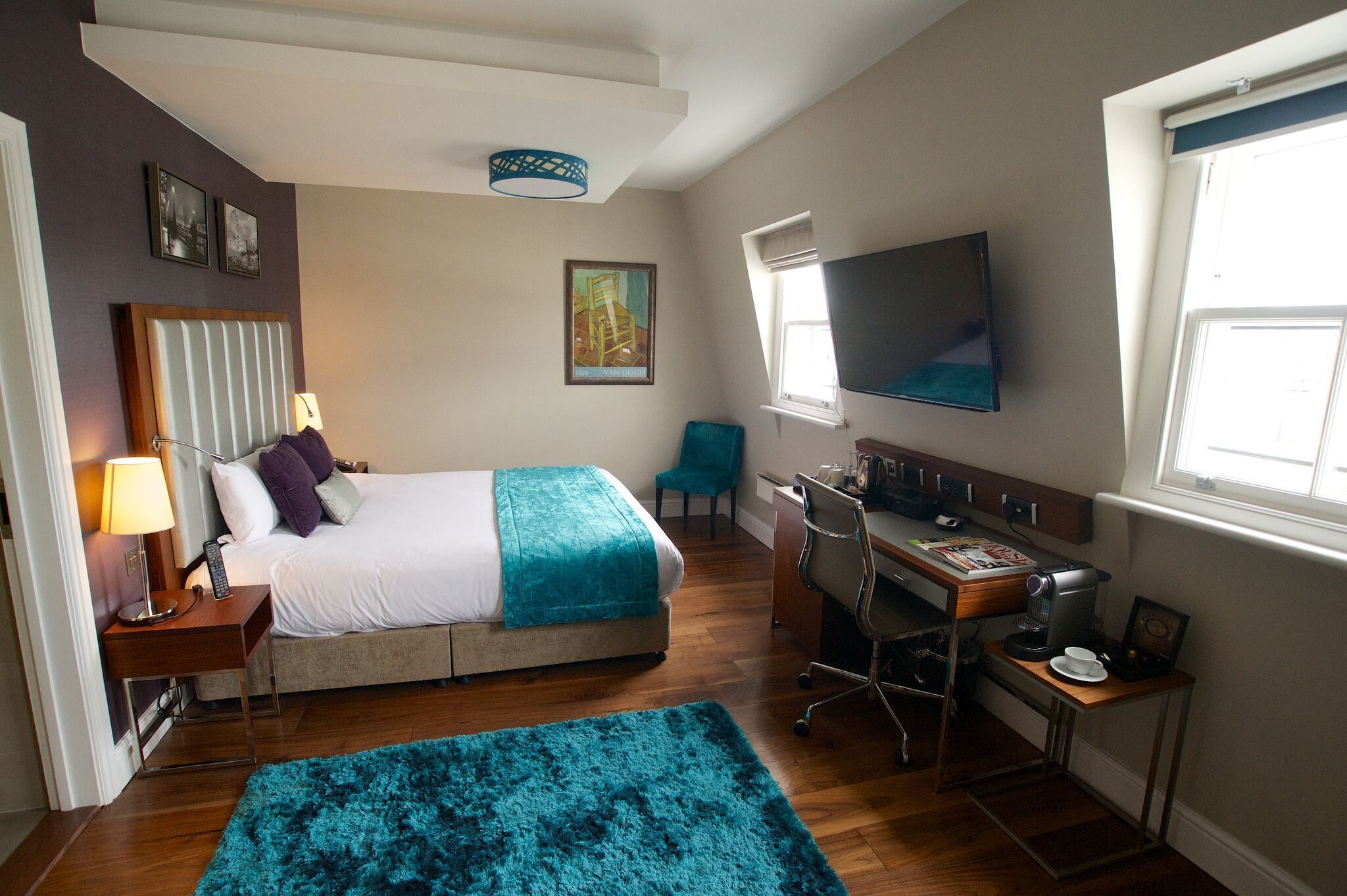 A hotel room with a bed, desk, chair, TV, and a window.